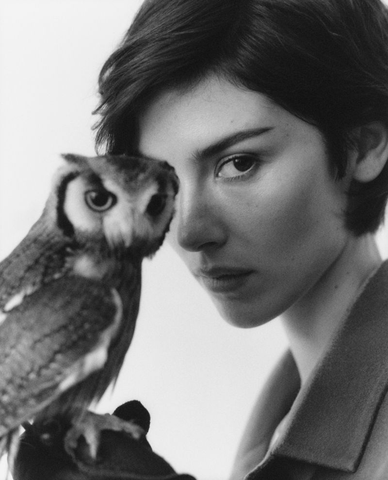 Portrait of a woman holding an owl close to her face in a black and white editorial shoot for Rolling Stone.