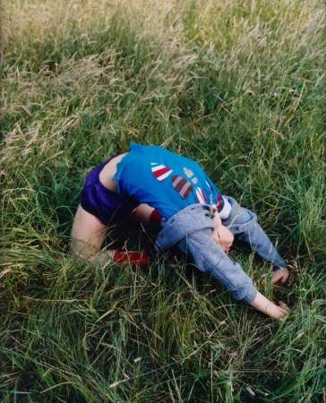 Child in a blue t-shirt and purple shorts performing a backbend in tall green grass for a Rolling Stone editorial shoot.