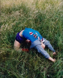 Child in a blue t-shirt and purple shorts performing a backbend in tall green grass for a Rolling Stone editorial shoot.