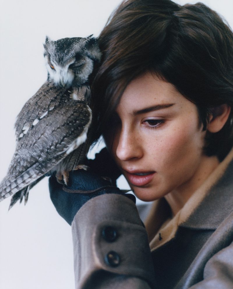 Close-up portrait of a woman with short dark hair holding a small owl resting against her head.