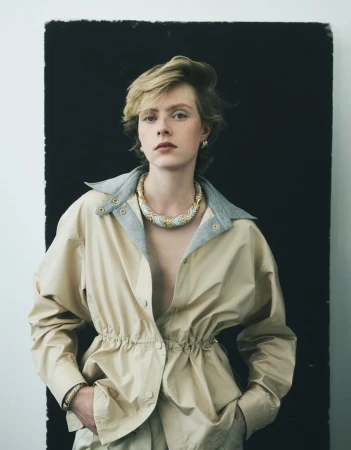 Model wearing a beige jacket and ornate necklace against a high-contrast black and white studio backdrop