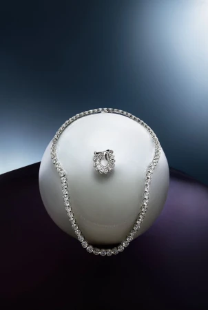Diamond tennis necklace and matching ring resting on a smooth white spherical surface against a gradient background.