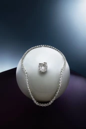 Diamond tennis necklace and matching ring resting on a smooth white spherical surface against a gradient background.