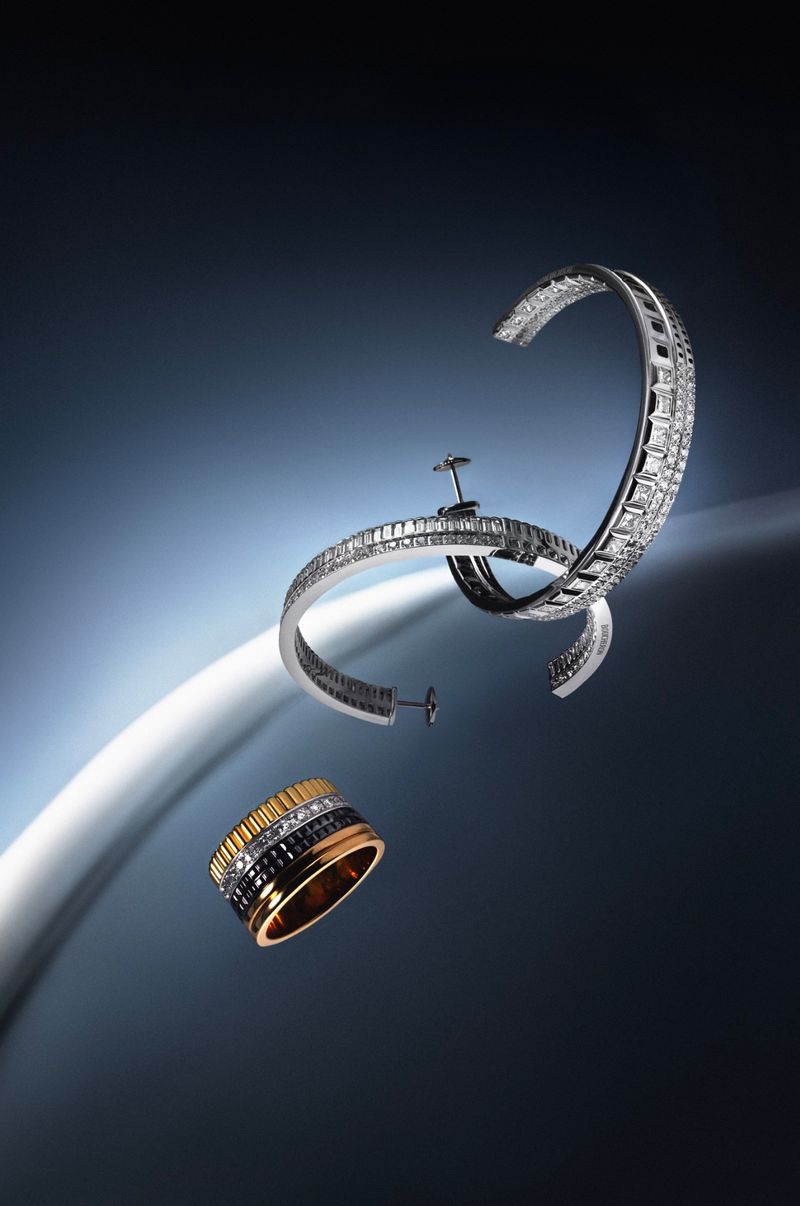 Floating silver diamond hoop earrings and a gold and black ring against a dark blue gradient studio background with a glowing curve