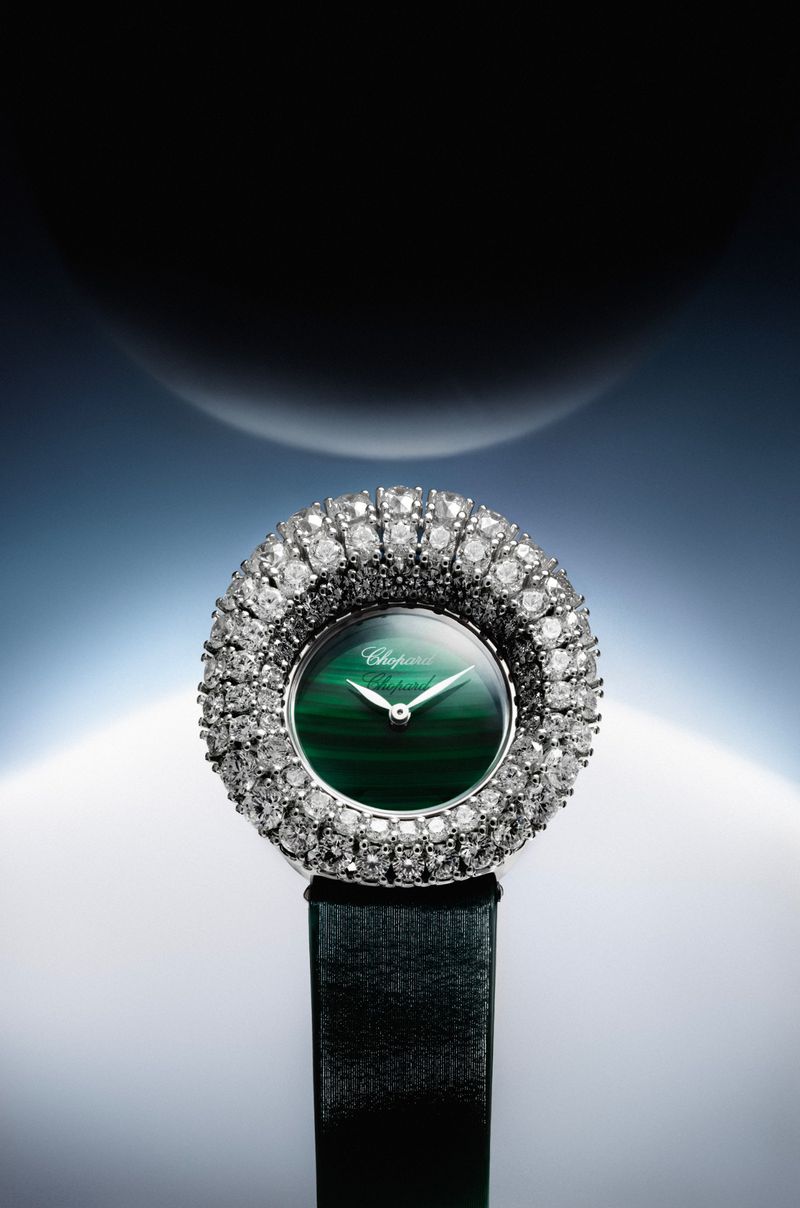 Luxury diamond wristwatch with a green dial against a dark glowing gradient background with abstract spherical elements