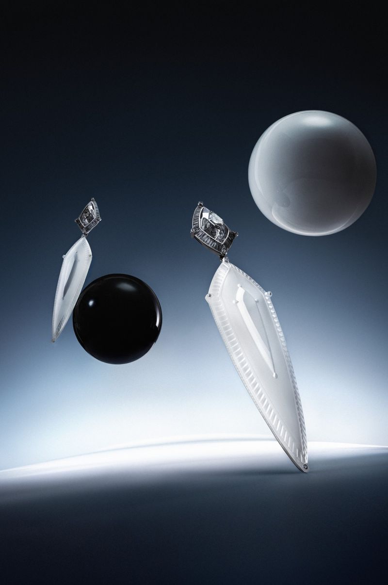 Floating avant-garde earrings and spherical orbs against a gradient white and dark blue studio backdrop.