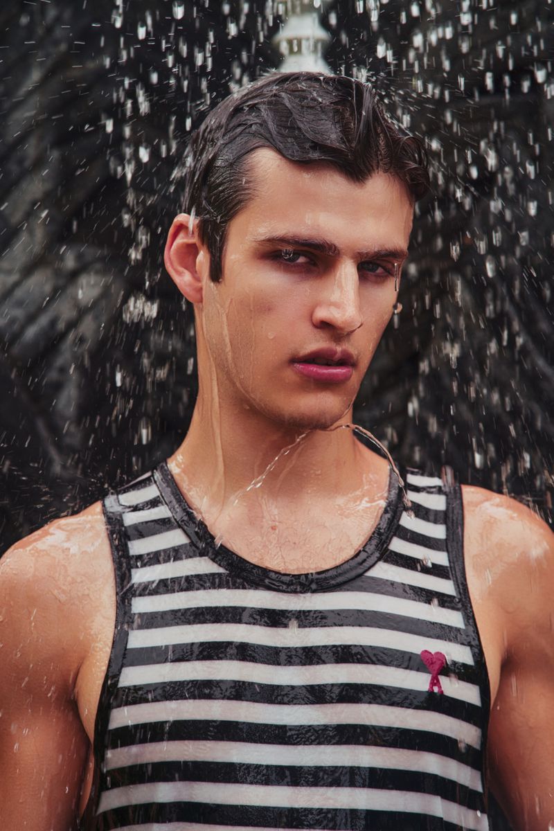 Man wearing a black and white striped tank top standing beneath cascading water from a fountain.