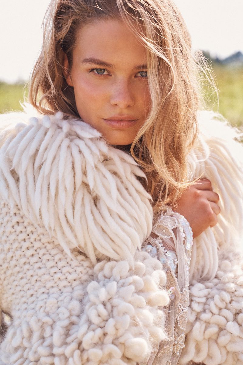 Model with blonde hair wearing a textured white knitted cardigan outdoors against a natural green landscape background
