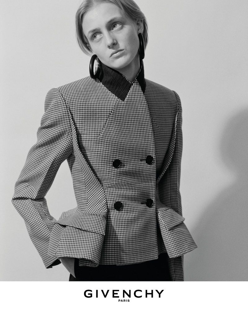 Model wearing a structured houndstooth double-breasted jacket and oversized hoop earrings against a plain background for Givenchy
