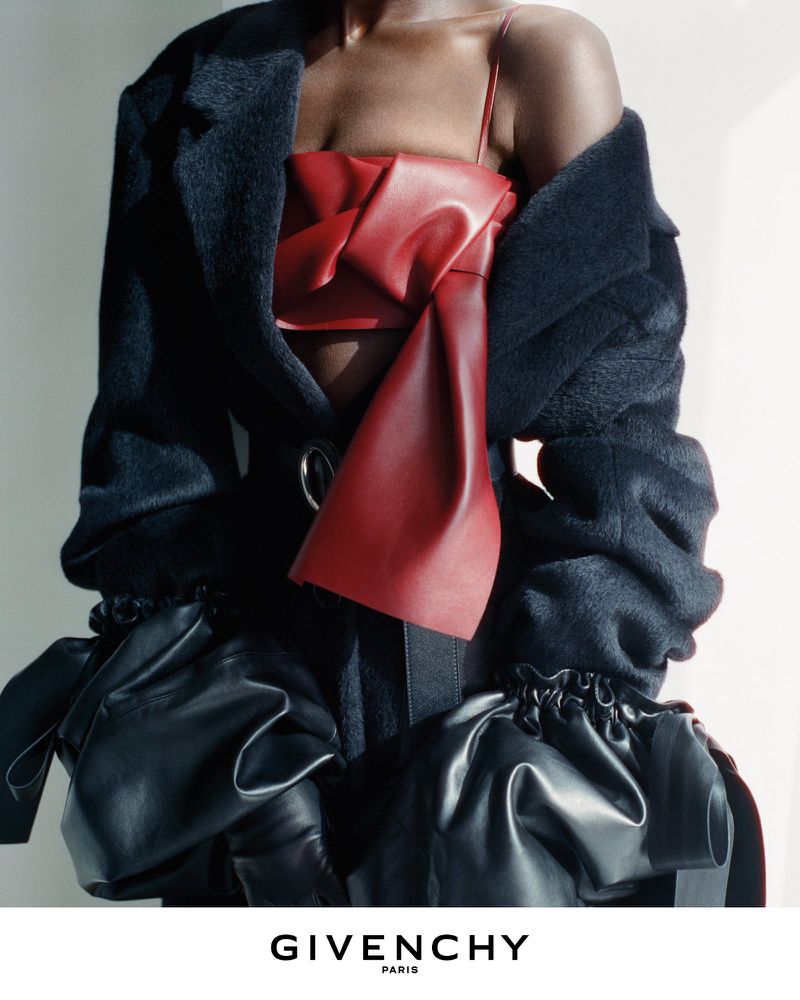 Model wearing a structured red top and black coat against a neutral background for Givenchy