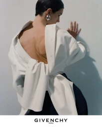 Model wearing a back-to-front white button-up shirt and large silver earring leaning against a plain white wall.