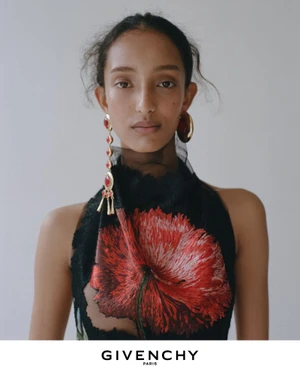 Model wearing a black top with a large red floral embroidery and statement earrings against a plain white wall