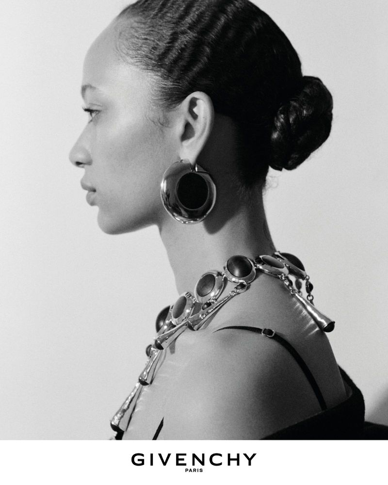 Profile portrait of a model wearing large silver statement earrings and a chunky link necklace for the Givenchy Winter 2026 campaign.