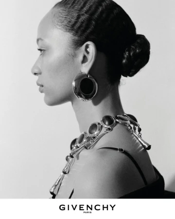 Profile portrait of a model wearing large silver statement earrings and a chunky link necklace for the Givenchy Winter 2026 campaign.