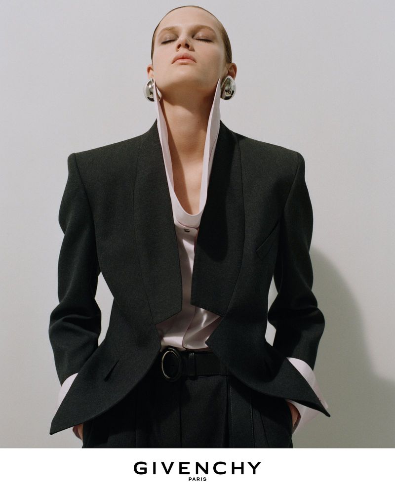 Model wearing a tailored black blazer and high-collared shirt against a white background for Givenchy