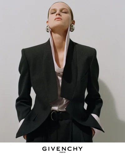 Model wearing a tailored black blazer and high-collared shirt against a white background for Givenchy