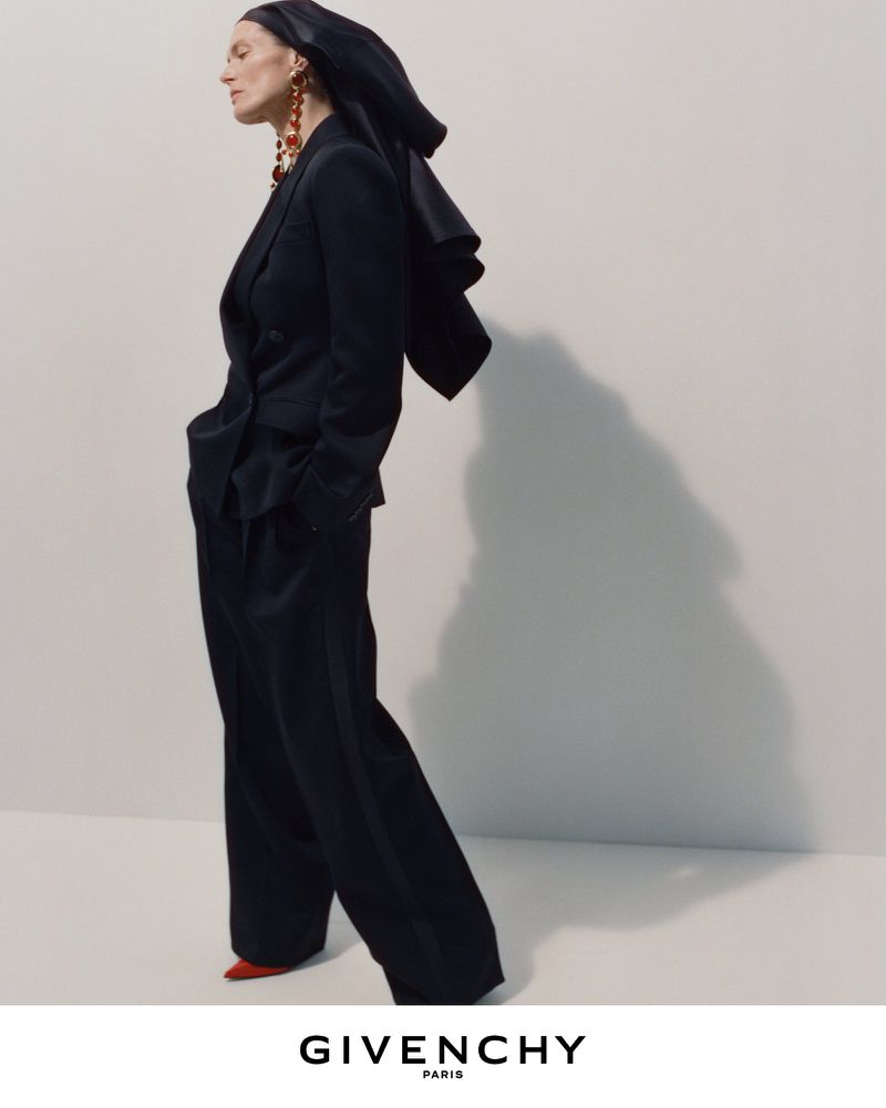 Model in black suit and hooded headwear posing against a plain backdrop with visible shadow for Givenchy Winter 2026 campaign.