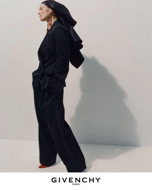 Model in black suit and hooded headwear posing against a plain backdrop with visible shadow for Givenchy Winter 2026 campaign.