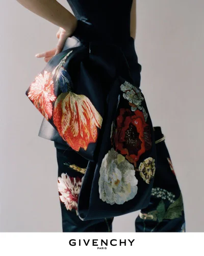 Close-up of a dark outfit featuring vibrant floral embroidery and a prominent bow detail against a neutral background.