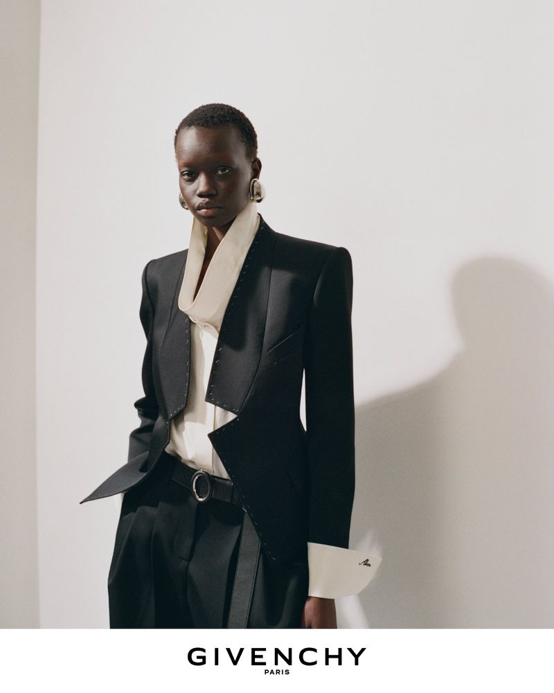 Model wearing a tailored black blazer and white collared shirt against a white wall for Givenchy Winter 2026 campaign.