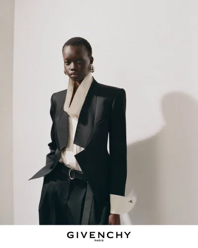 Model wearing a tailored black blazer and white collared shirt against a white wall for Givenchy Winter 2026 campaign.