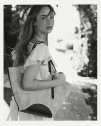 Jennifer Lawrence carrying a patterned Dior tote bag outdoors in a black and white portrait.