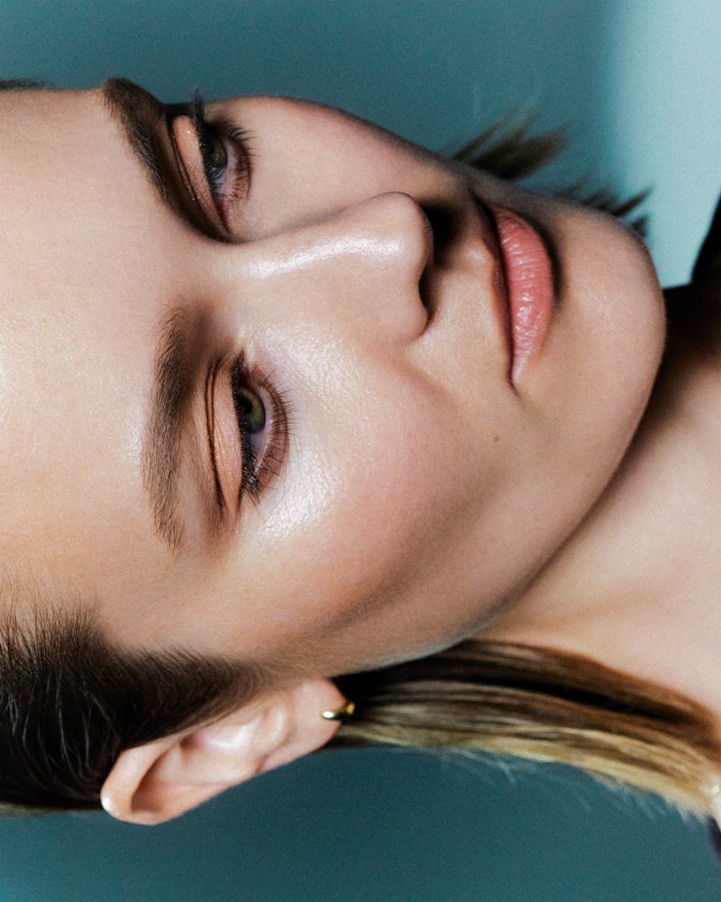 Close-up beauty portrait of a woman wearing warm eyeshadow against a teal background for Saie Beauty