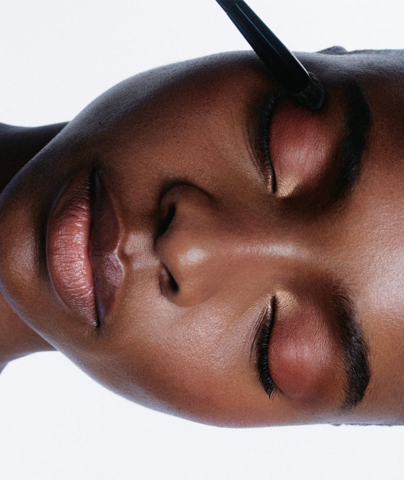 Close-up beauty portrait of a Black woman having eyeshadow applied with a brush against a white background