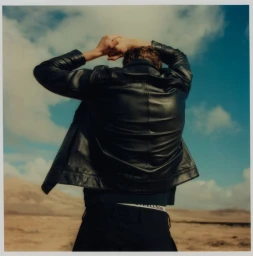 Man wearing a black leather jacket with hands behind his head against a desert landscape and cloudy sky for Strellson.