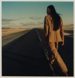 Model with long dark hair wearing a camel suit walking along an open desert road at sunset for Strellson