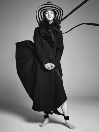 Model wearing a black coat and striped wide-brimmed hat against a grey seamless background for Harper's Bazaar Italia