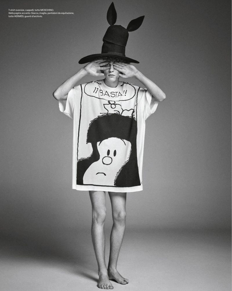 Model in graphic print t-shirt and tall black hat covering eyes against a grey studio backdrop