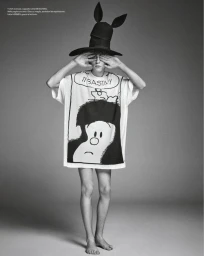 Model in graphic print t-shirt and tall black hat covering eyes against a grey studio backdrop