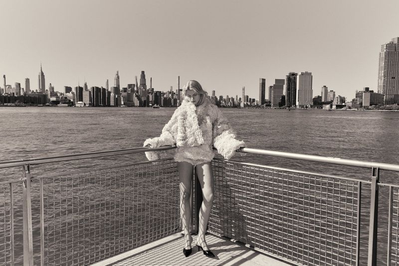 Model Tinka Carleton-Smith posing on a waterfront railing against a city skyline for Quiet Motion Issue 8