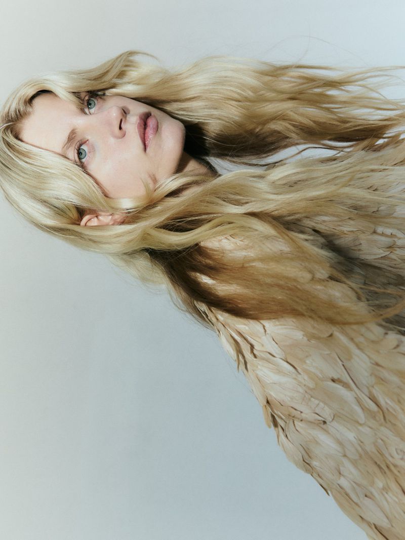 Portrait of a blonde woman wearing a textured feathered top against a plain white studio background.