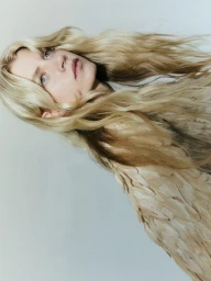 Portrait of a blonde woman wearing a textured feathered top against a plain white studio background.