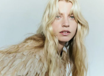 Close-up portrait of a blonde model with feathered garment against a neutral background for Quiet Motion