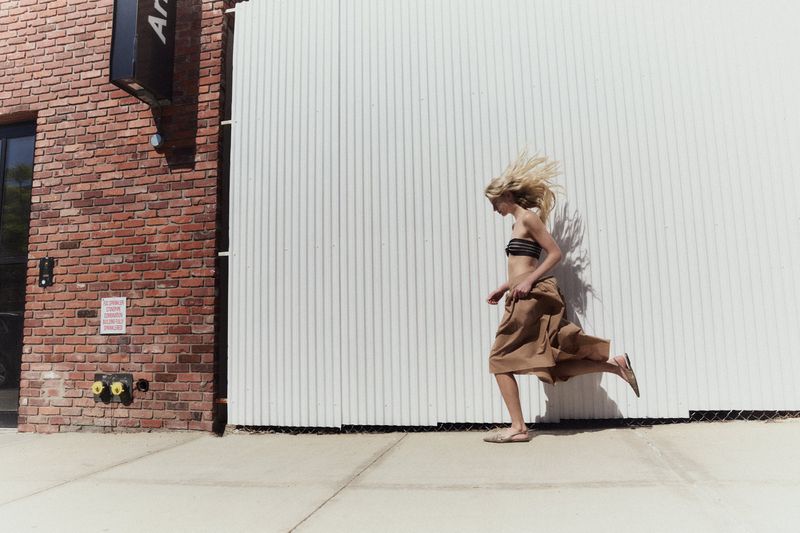 A blonde model running past a white corrugated wall and red brick building for Modern Road.