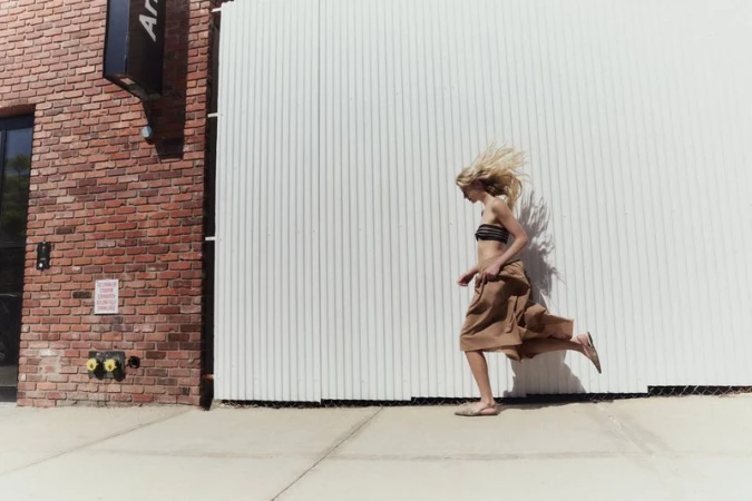 A blonde model running past a white corrugated wall and red brick building for Modern Road.