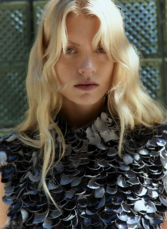 Close-up portrait of a blonde female model wearing a dark textured top against a patterned background for Quiet Motion