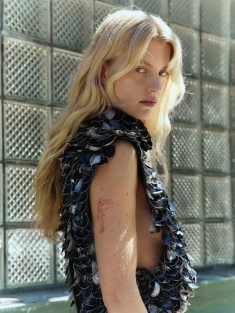 Blonde woman wearing a textured dark sequined sleeveless top against a glass block wall