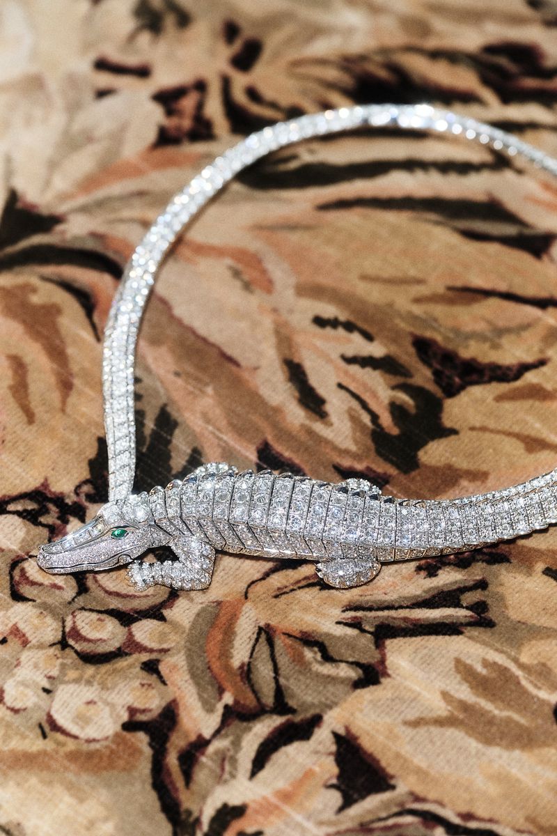 Close-up shot of an intricate diamond alligator necklace resting on a patterned fabric surface.