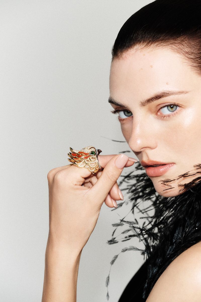 Close-up portrait of a woman wearing an intricate bird ring and black feather garment against a seamless light background