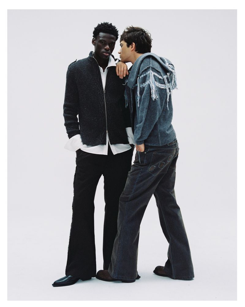Two male models posing together against a plain white studio backdrop, wearing contemporary casual jackets and trousers.