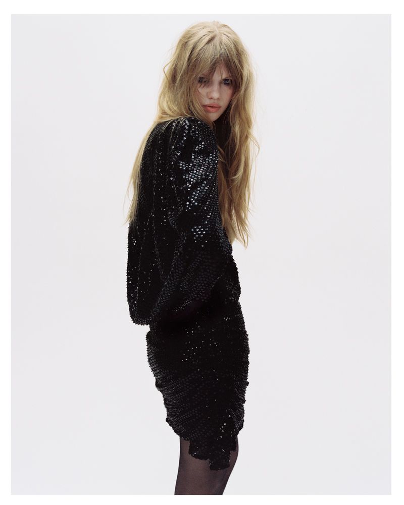 Model with long blonde hair wearing a black sequined dress against a white seamless background