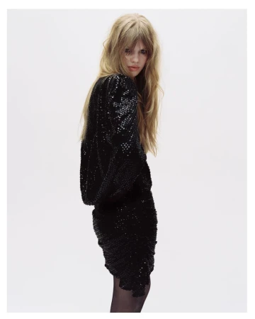 Model with long blonde hair wearing a black sequined dress against a white seamless background