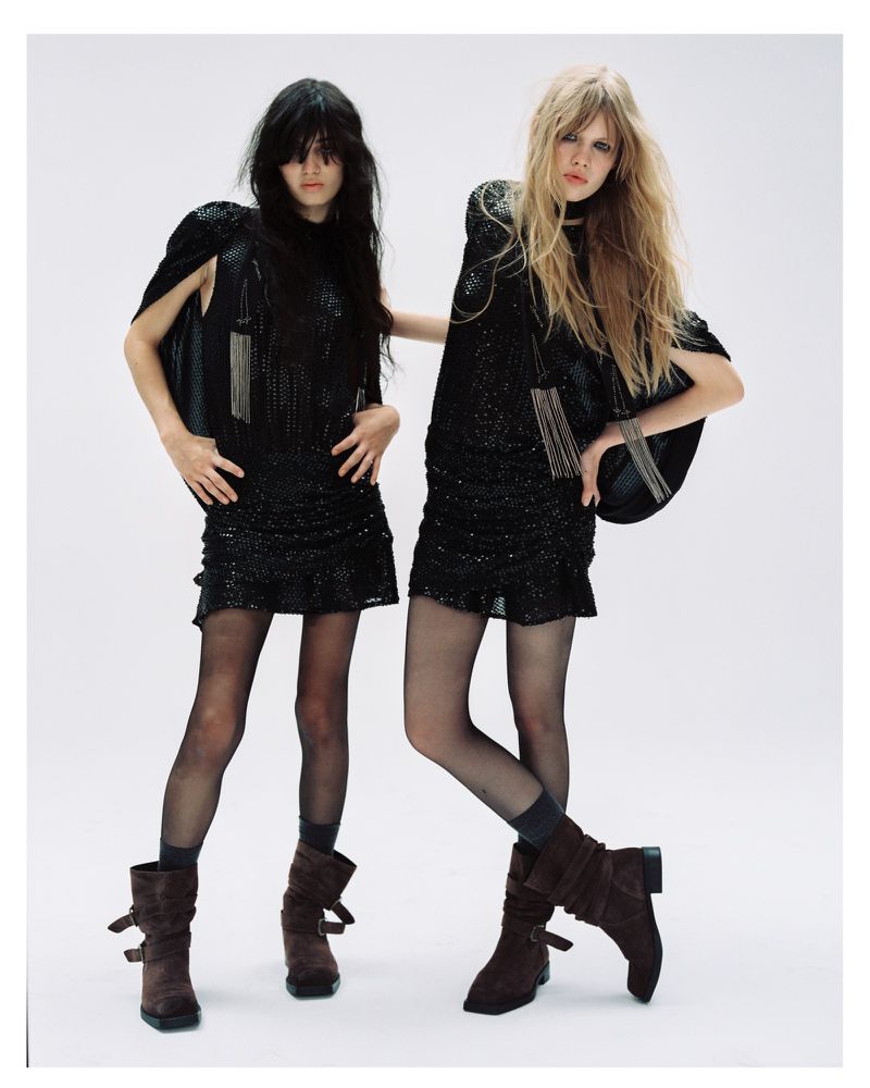 Two female models wearing black embellished dresses and brown boots against a white studio background.