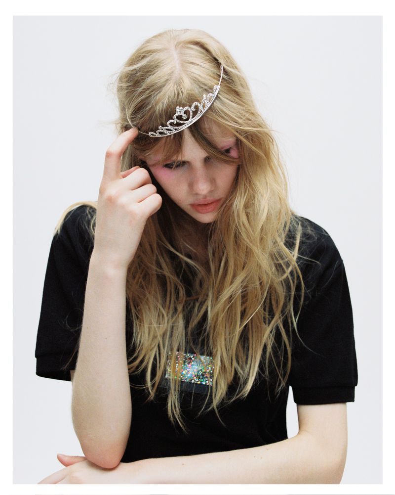 Blonde model wearing a tiara and black t-shirt against a plain white background