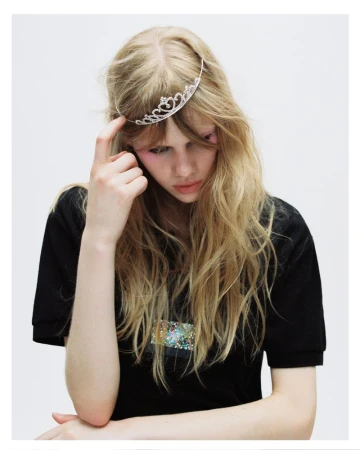 Blonde model wearing a tiara and black t-shirt against a plain white background
