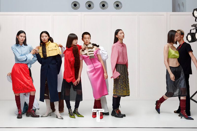 Group of female models in colorful designer outfits posing against a white studio wall during a photo shoot for T Magazine China
